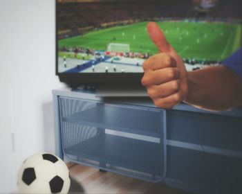 Close-up of man showing thumbs up against television set
