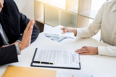 Midsection of businesswoman bribing with businessman at desk