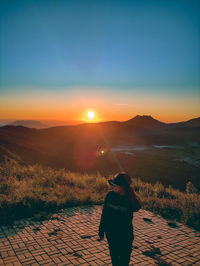 Rear view of woman standing on mountain against sky during sunset