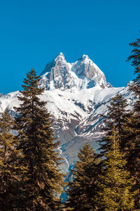 Low angle view of snowcapped mountains against clear blue sky