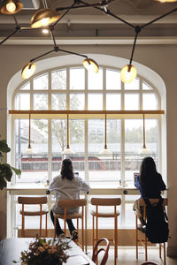 Rear view of businesswomen working on laptop while sitting on chair near window at coworking office