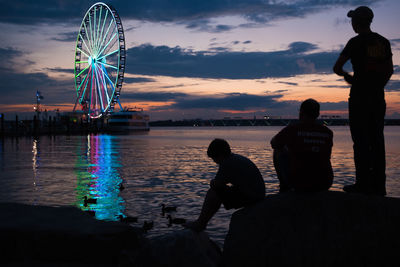 Rear view of silhouette people with ferris wheel in sea against sky