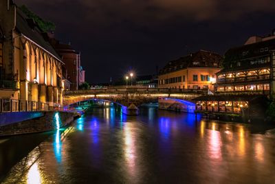 Illuminated bridge over river amidst buildings in city at night