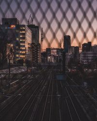 High angle view of railroad tracks by buildings against sky seen through fence