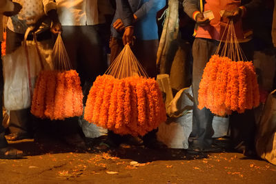 Low section of men holding floral garlands for sale while standing on footpath