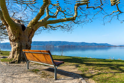 Empty bench by lake against sky