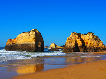 Rock formation on beach against clear blue sky