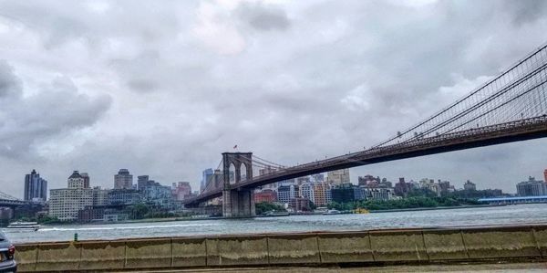 Bridge over river by buildings against sky