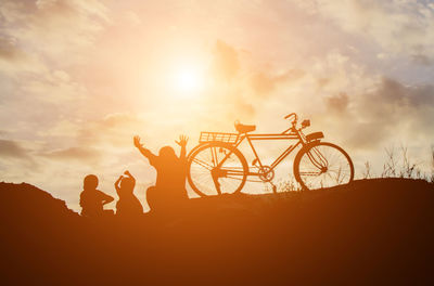 Silhouette people riding bicycle against sky during sunset