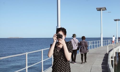 Rear view of people photographing sea against clear sky