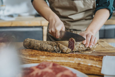 Female chef cutting salami on cutting board while standing in kitchen