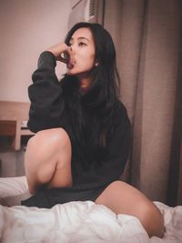 Young woman sitting on bed at home