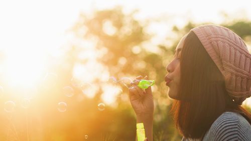 Close-up of young woman blowing bubbles during sunny day at public park