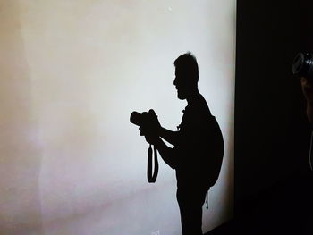 Side view of silhouette man photographing against wall