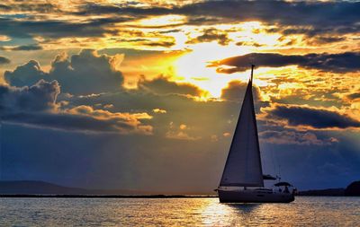 Silhouette sailboat sailing on sea against dramatic sky