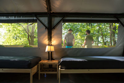 Rear view of hikers standing in forest seen through tent window