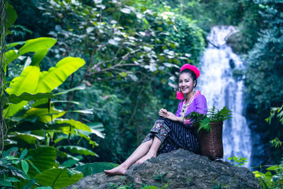 Portrait of young woman sitting on rock against trees