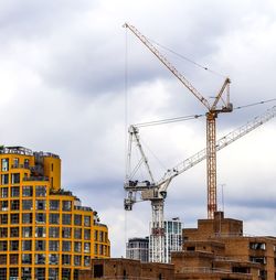 Low angle view of crane by building against sky