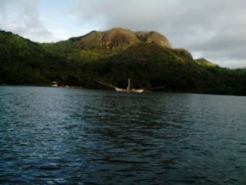 Scenic view of sea by mountain against sky