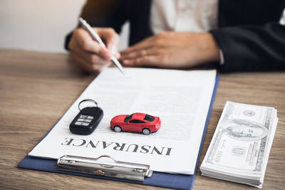 Midsection of person holding pen over paper with text by car key and paper currency on table