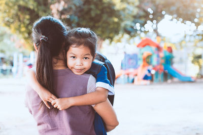 Rear view of mother carrying daughter while standing in playground