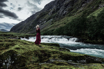 Rear view of woman standing on rock against mountain