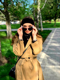 Portrait of young woman wearing sunglasses standing against trees