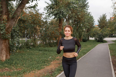 Young attractive girl in sports tight clothes running in the park among green foliage