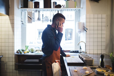 Side view of mature chef talking on mobile phone while standing at kitchen counter in restaurant