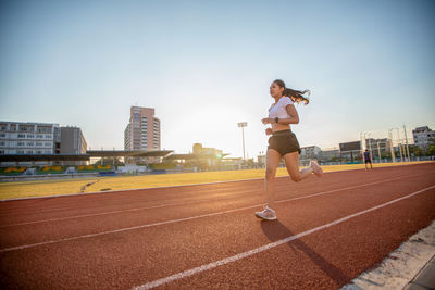 Full length of woman running on track against sky