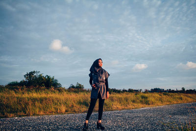Full length of woman looking away while standing on road against sky