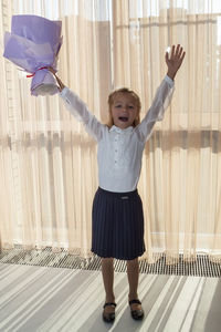 Full length of smiling girl standing against curtain