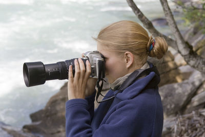 Side view of young woman photographing with camera by sea