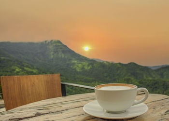 Coffee cup on table against sky during sunset