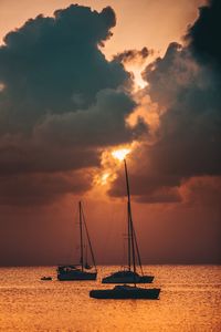 Silhouette boats in sea against dramatic sky
