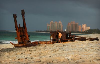 People by shipwreck at beach against sky