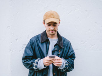 Portrait of smiling young man using phone against white wall