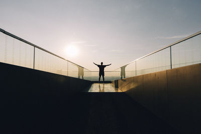 Silhouette person standing on pole against sky