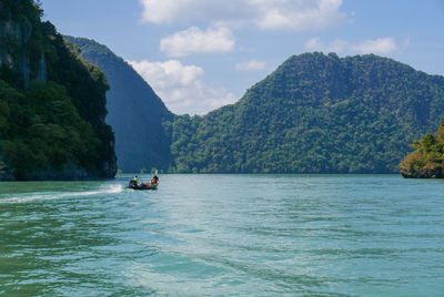 Boat sailing on sea by mountains against sky