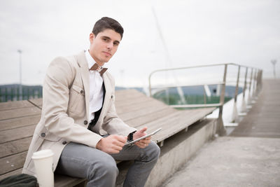 Portrait young man using digital tablet while sitting on bench