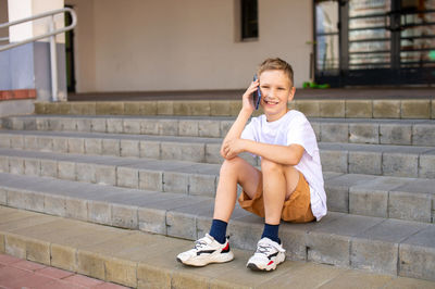 The boy sits on the steps and takes a selfie