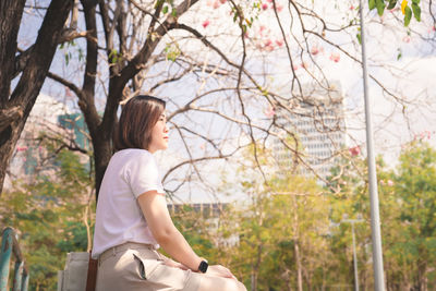 Woman looking away while sitting on tree