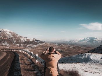 Rear view of man photographing while standing by railing during winter