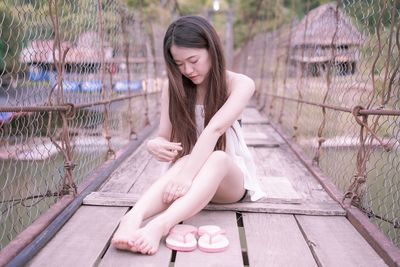 Beautiful young woman sitting on footbridge over lake