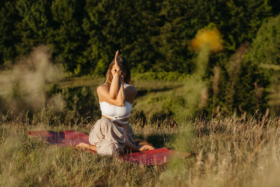 Young woman practicing yoga on the mat outdoors at sunset with beautiful landscape on the background