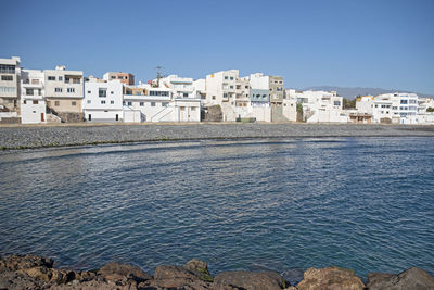 Buildings by sea against clear blue sky