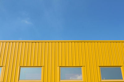 Low angle view of yellow building against clear blue sky