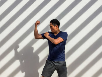 Man flexing muscle while standing against wall