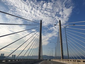 Low angle view of suspension bridge against cloudy sky