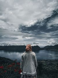 Rear view of woman standing by lake against sky